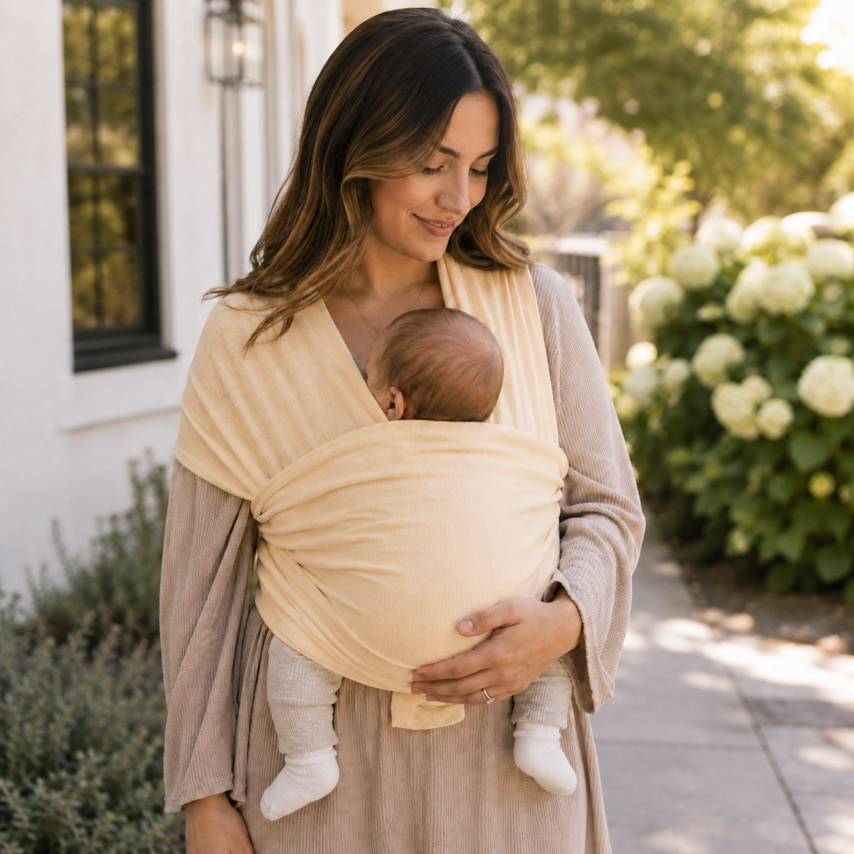 Cream organic baby wrap carrier draped over shoulder with infant in facing-in carry