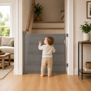 Grey retractable mesh stair gate at doorway, with toddler standing nearby