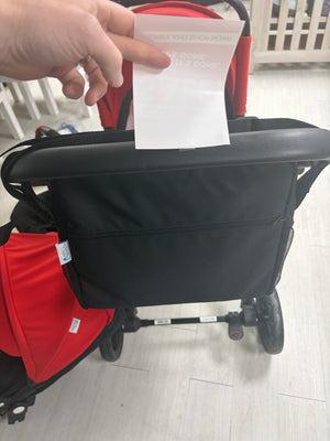 Black changing bag attached to stroller frame, with red stroller seat panel behind