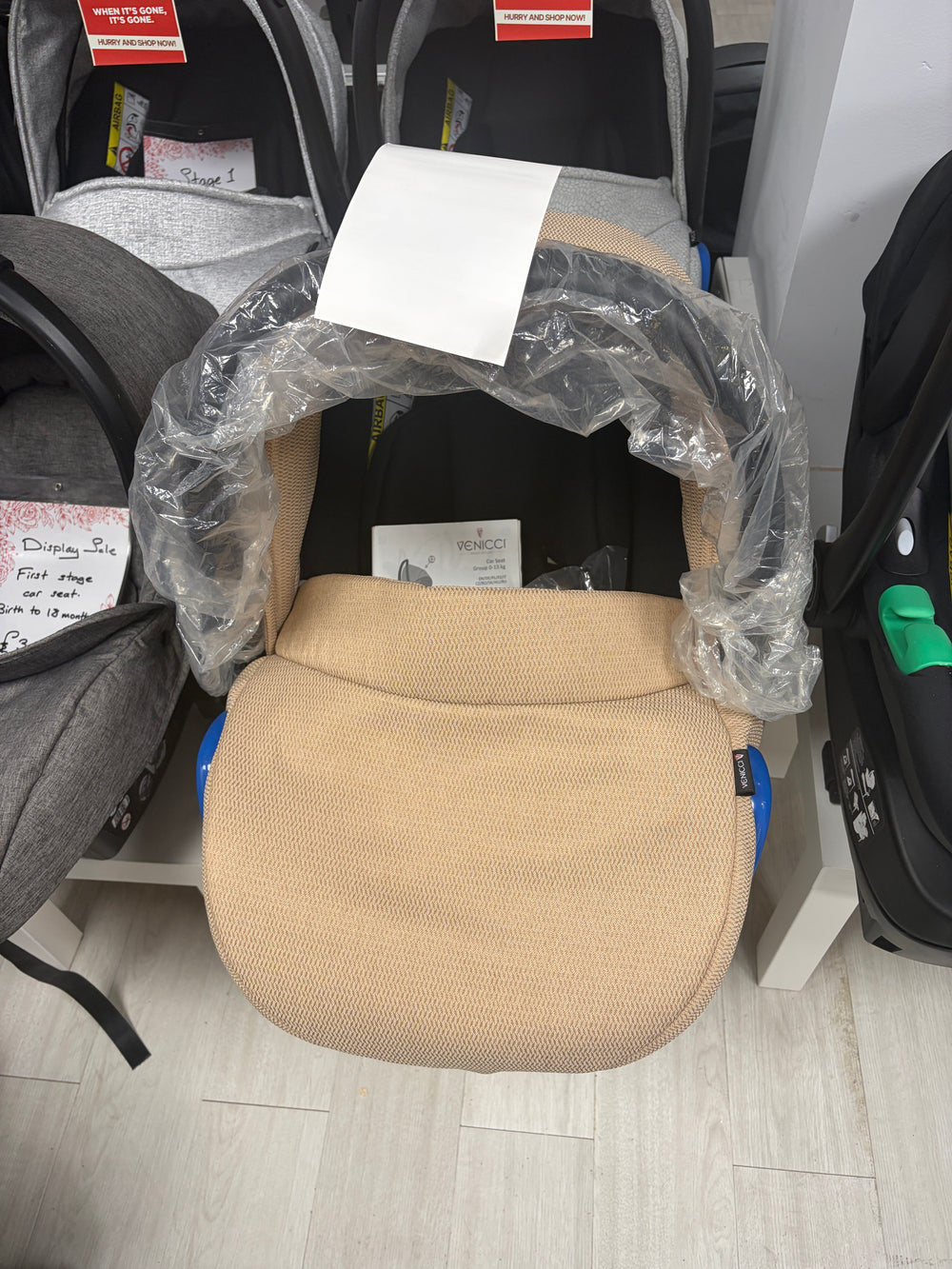 Cream newborn car seat with padded insert, wrapped in protective plastic