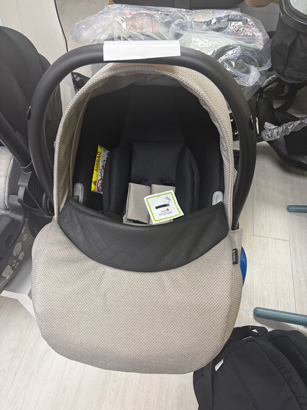Beige newborn car seat carrier with black canopy and safety harness, front view
