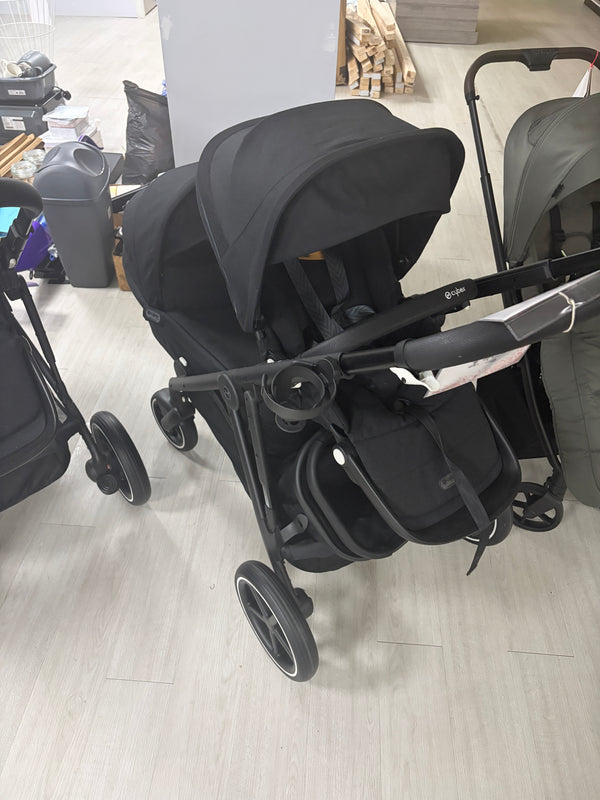 Double stroller with black seat unit and canopy, front wheels and handlebars visible