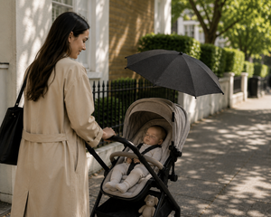 Black baby stroller parasol held above a seated infant in the bassinet