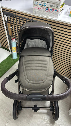 Gray stroller bassinet with padded inner liner, arch handle, and black chassis wheels