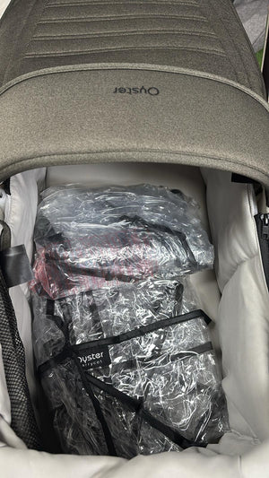 Gray stroller canopy open, showing bundled accessories in clear plastic bags