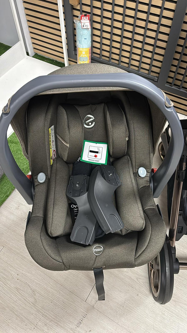 Gray infant car seat with head support and harness, mounted on stroller base frame