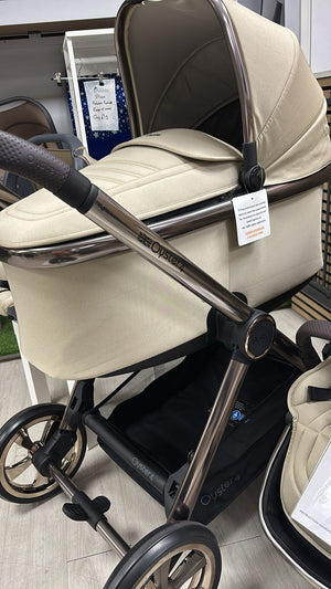 Beige stroller seat with dark handle and wheels, angled close-up